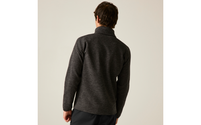 Rückenansicht einer Person mit kurzen dunklen Haaren, die einen dunkelgrauen Pullover mit Stehkragen und schwarze Hosen vor hellem Hintergrund trägt