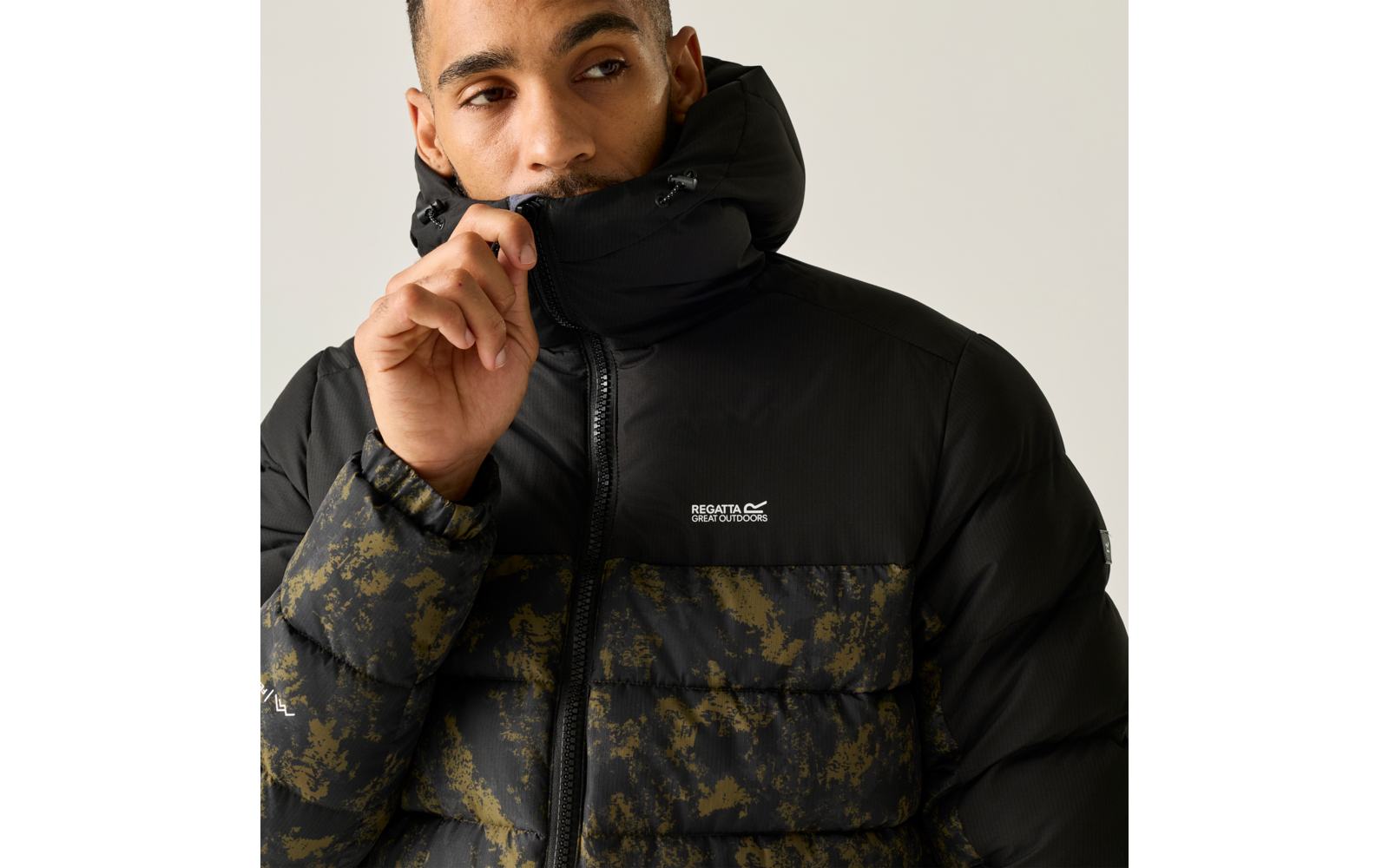 Person zieht den Reißverschluss einer schwarzen Steppjacke mit hohem Kragen hoch, unterer Teil mit camouflageähnlichem Muster