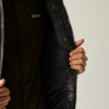 Zwei Hände halten eine geöffnete Jacke; sichtbar: dunkles, gemustertes Innenfutter mit Pflegepiktogrammen und ein dunkelgrüner Reißverschluss-Pullover