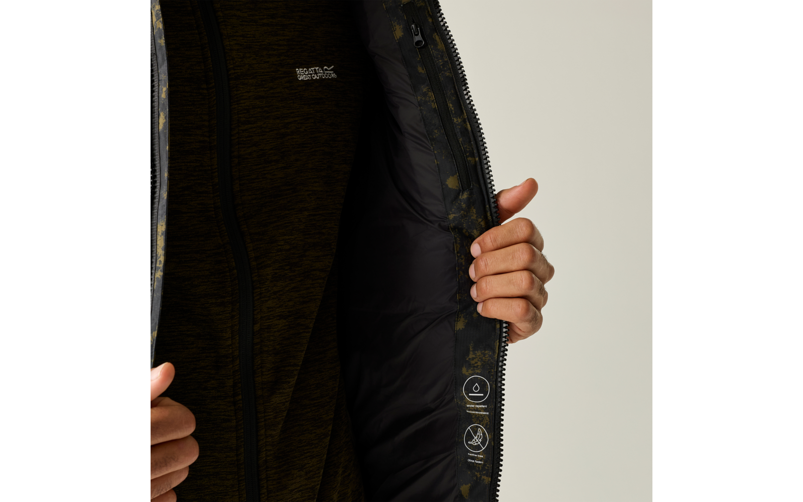 Zwei Hände halten eine geöffnete Jacke; sichtbar: dunkles, gemustertes Innenfutter mit Pflegepiktogrammen und ein dunkelgrüner Reißverschluss-Pullover
