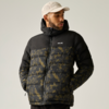 Person trägt schwarze gesteppte Jacke mit olivgrünem Muster und Kapuze, Hände in den Taschen, beige Baseballcap, vor hellem einfarbigem Hintergrund