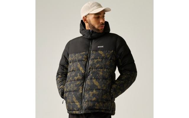 Person trägt schwarze gesteppte Jacke mit olivgrünem Muster und Kapuze, Hände in den Taschen, beige Baseballcap, vor hellem einfarbigem Hintergrund