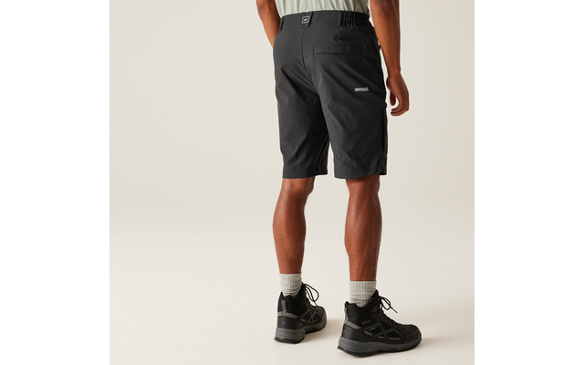 Person von hinten, knielange schwarze Shorts, helles T-Shirtansatz sichtbar, weiße Socken, schwarze Schnürschuhe, heller neutraler Hintergrund