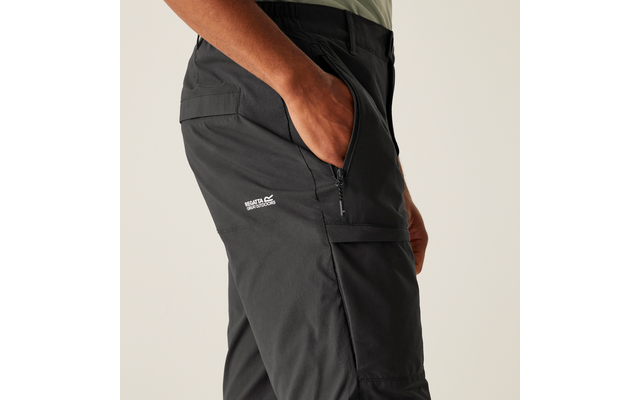 Seitliche Ansicht einer Person mit der rechten Hand in der Hosentasche, schwarze Hose mit Reißverschlusstasche und weißem Logo auf dem Oberschenkel