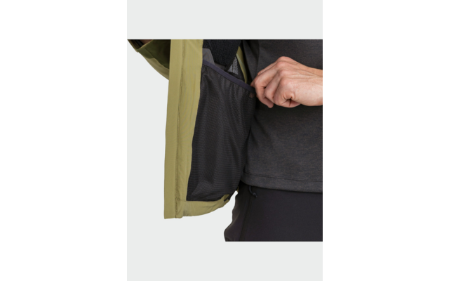 Main ouvrant la poche intérieure d'une veste vert olive; doublure en maille noire visible; partie d'un t-shirt sombre et d'un pantalon sombre