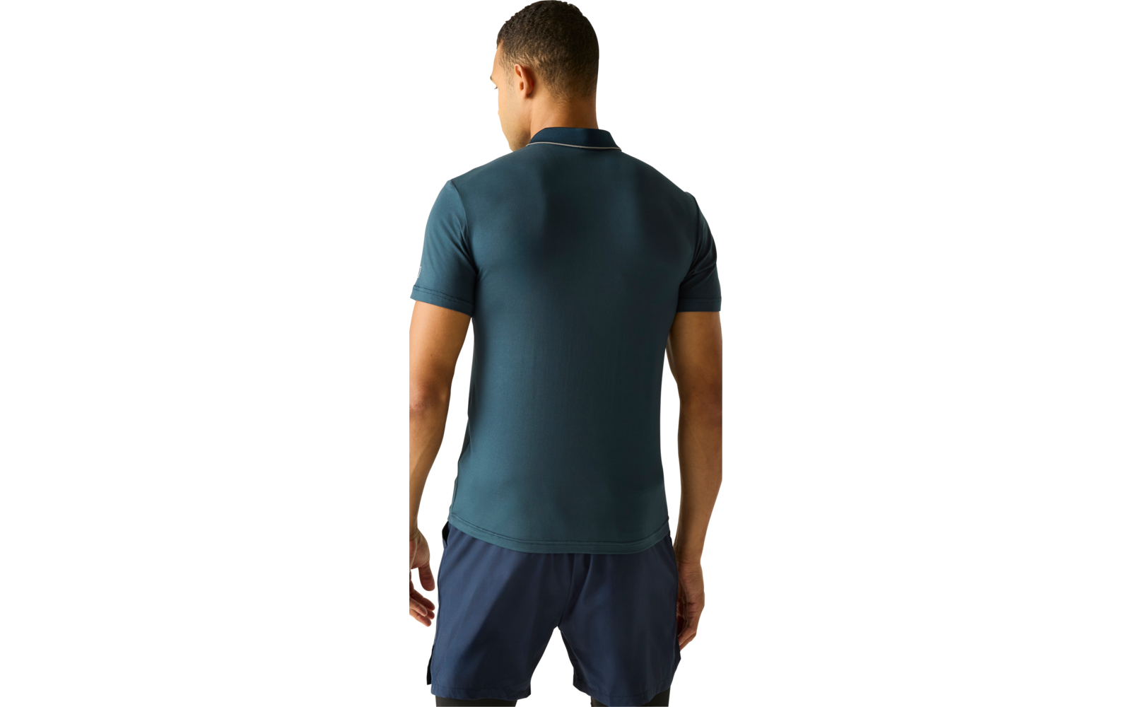 Person von hinten, trägt ein blaugrünes Poloshirt und dunkelblaue Shorts vor hellem einfarbigem Hintergrund