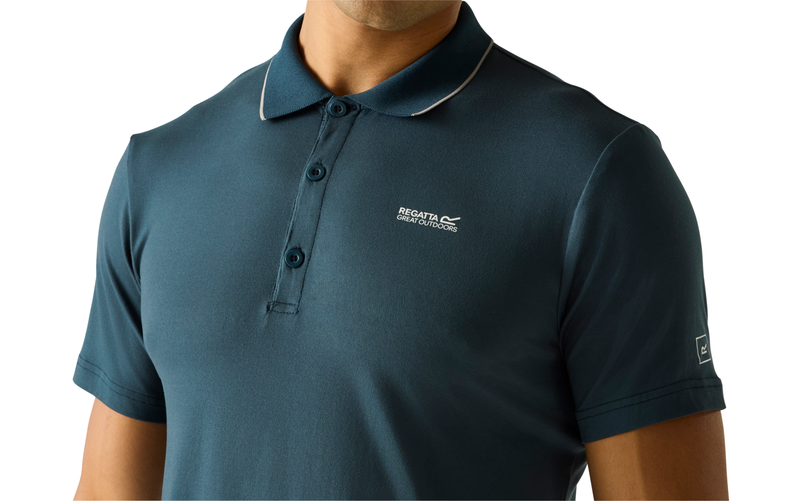 Person von Brusthöhe aufwärts, trägt dunkel-türkis-blaues Polohemd mit drei Knöpfen und kleinem weißen Logo auf der linken Brust, heller einfarbiger Hintergrund