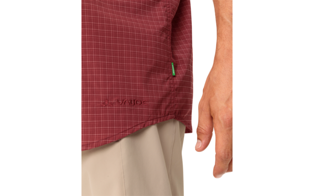 Close-up van de onderkant van een donkerrood geruit overhemd met een klein groen stoffen label en donkere borduursels, rechterarm en hand en beige broek