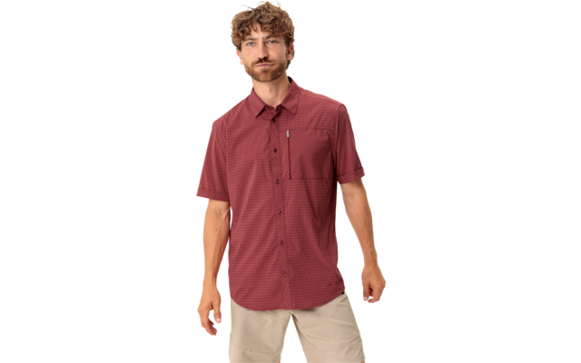 Man met krullend lichtbruin haar en baard, draagt een rood overhemd met korte mouwen en patroon en lichtbeige korte broek, staand voor een witte achtergrond