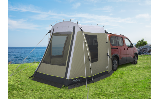 Rotes Auto mit grauem Anbauzelt auf grüner Wiese am Meer