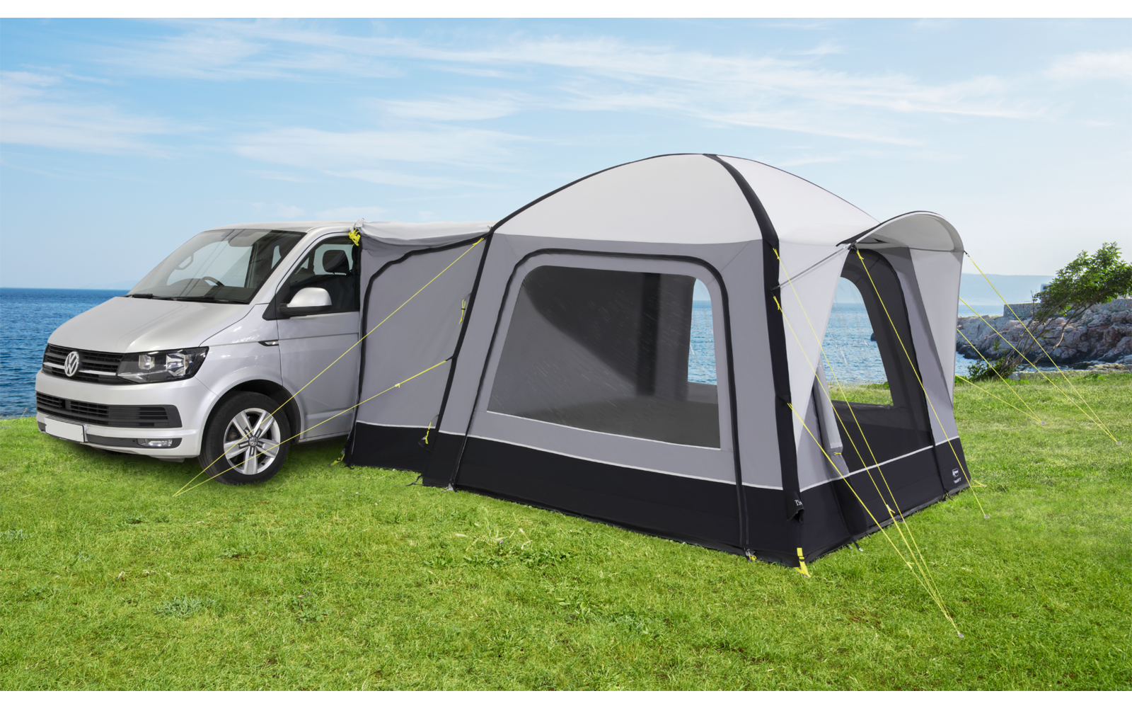 Weißer Camper Van mit angebautem großem grauem und schwarzem Zelt auf grünem Rasen unter blauem Himmel