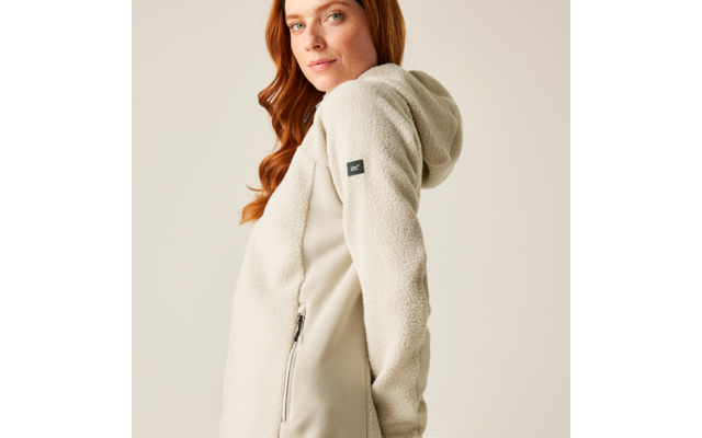 Frau mit langen roten Haaren trägt eine beige Kapuzenjacke und blickt zur Seite