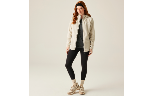 Frau mit langen roten Haaren trägt eine beige Jacke, graues Oberteil, schwarze Leggings und beige Stiefeletten