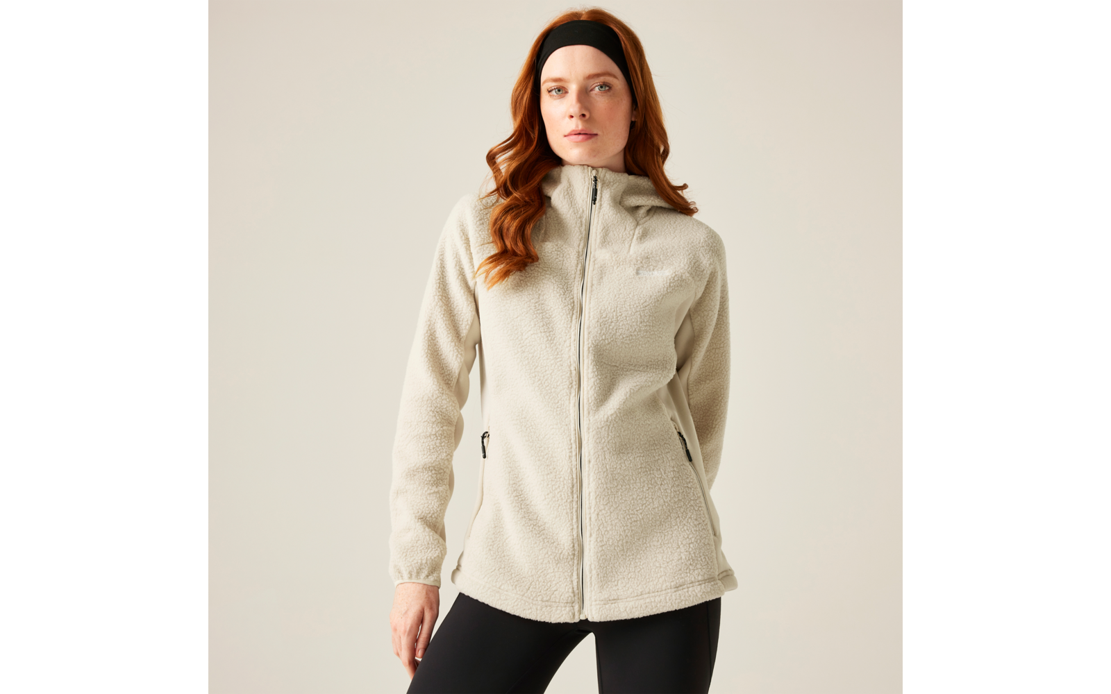 Frau mit langen roten Haaren trägt eine beige Jacke und schwarze Hose