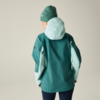 Person von hinten in grüner Jacke mit hellmintfarbener Kapuze und Ärmelfeldern, grüne Strickmütze, dunkle Hosen, heller neutraler Hintergrund