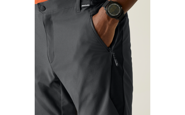 Nahaufnahme des Hüftbereichs: rechte Hand in Reißverschlusstasche einer dunkelgrauen Hose, digitale Armbanduhr am Handgelenk