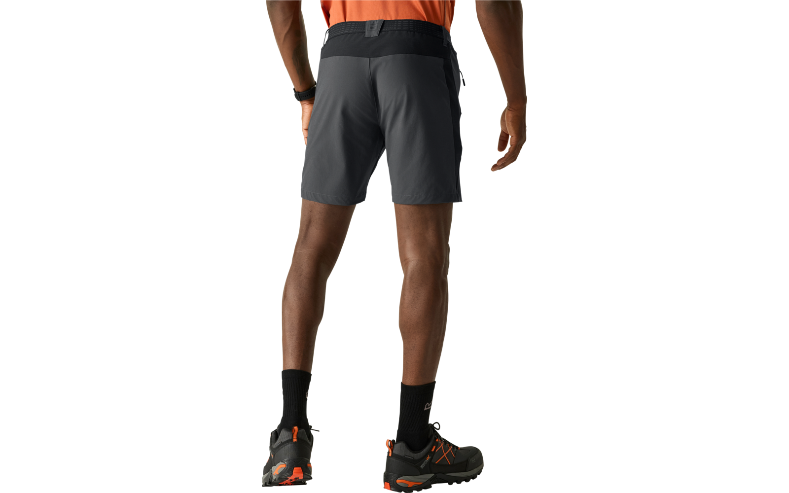 Person von hinten, dunkelgraue Shorts mit schwarzem Bund, orange Oberteil, schwarze Sportsocken, schwarze Sportschuhe mit orangefarbenen Details, heller Hintergrund