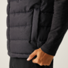 Nahaufnahme einer Hand am Saum einer schwarzen Steppweste ohne Ärmel über einem dunklen Langarmshirt und schwarzen Hosen