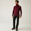 Ein Mann steht vor einem hellen Hintergrund, trägt einen roten Pullover und schwarze Hose