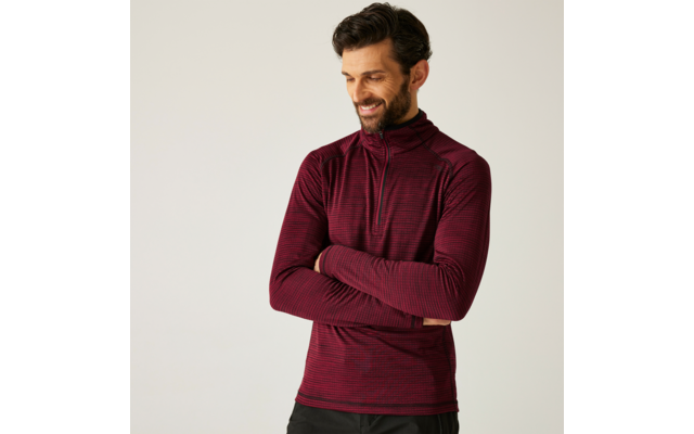 Mann mit bordeauxrotem Pullover, der lächelnd seitlich schaut und die Arme verschränkt hat