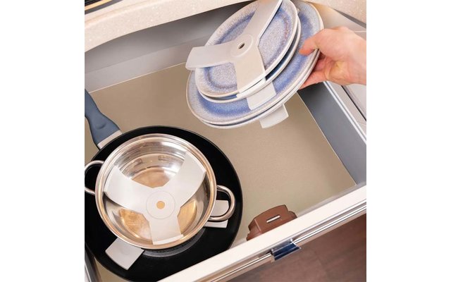 Hand holding three round blue speckled objects with white holding clips over an open drawer; inside the drawer a stainless steel pot with lid on a beige liner; drawer edges visible