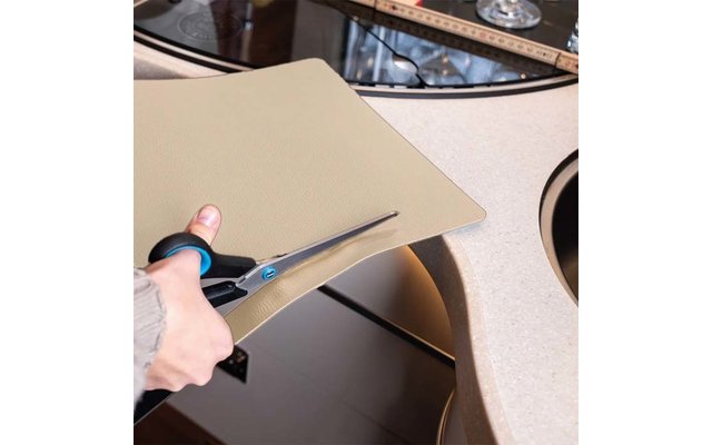 Hand cutting a beige mat with scissors over a sink