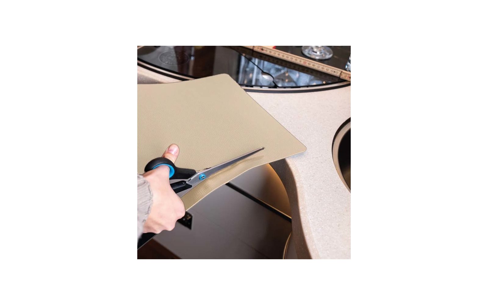 Hand cutting a beige mat with scissors over a sink