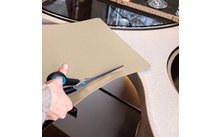 Hand schneidet mit Schere eine beige Matte über der Spüle
