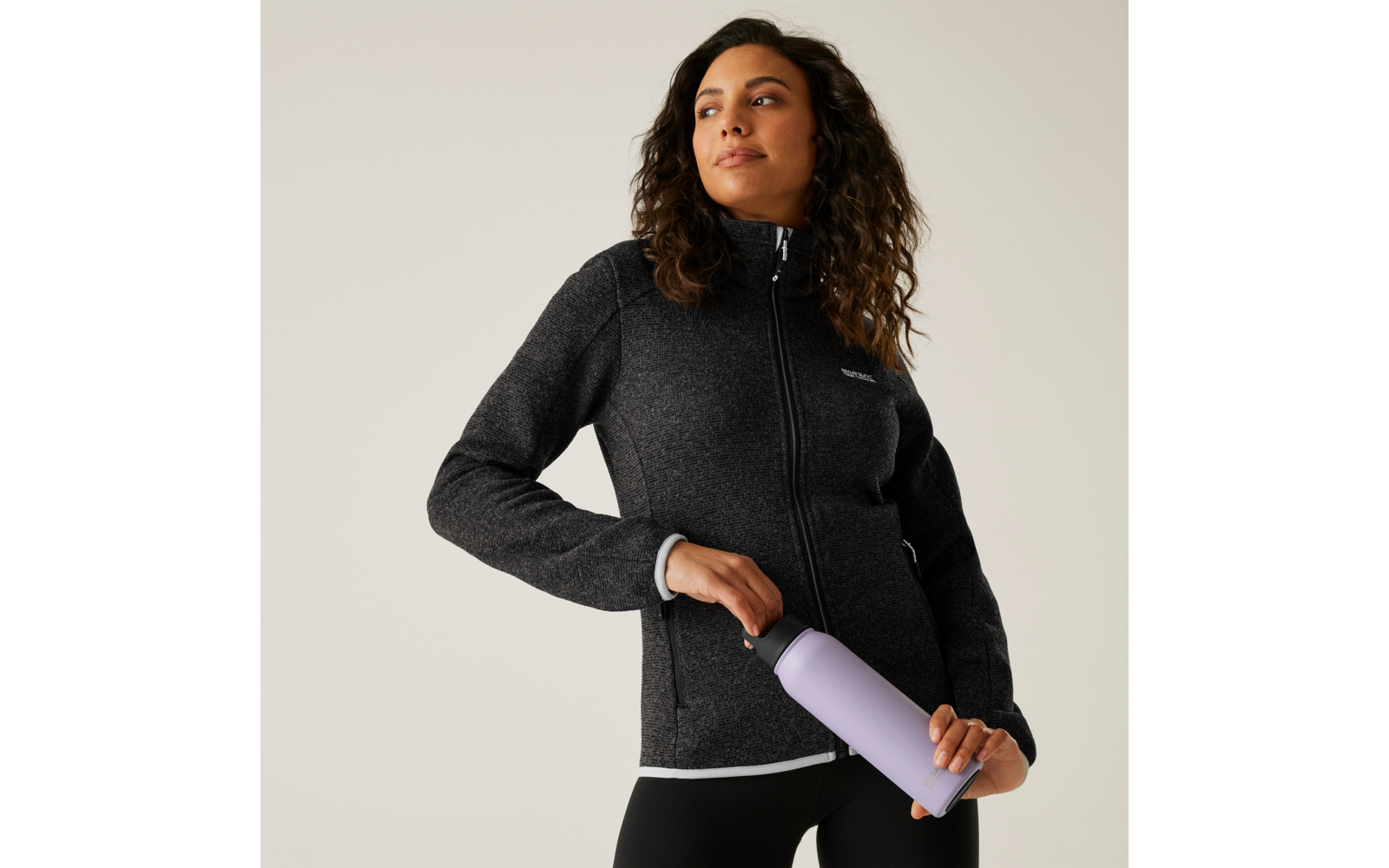Frau mit lockigem Haar trägt schwarzen Pullover und hält eine rosa Sportflasche in der Hand