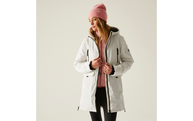 Frau mit rosa Mütze trägt helle Jacke und schwarzen Pullover vor hellem Hintergrund