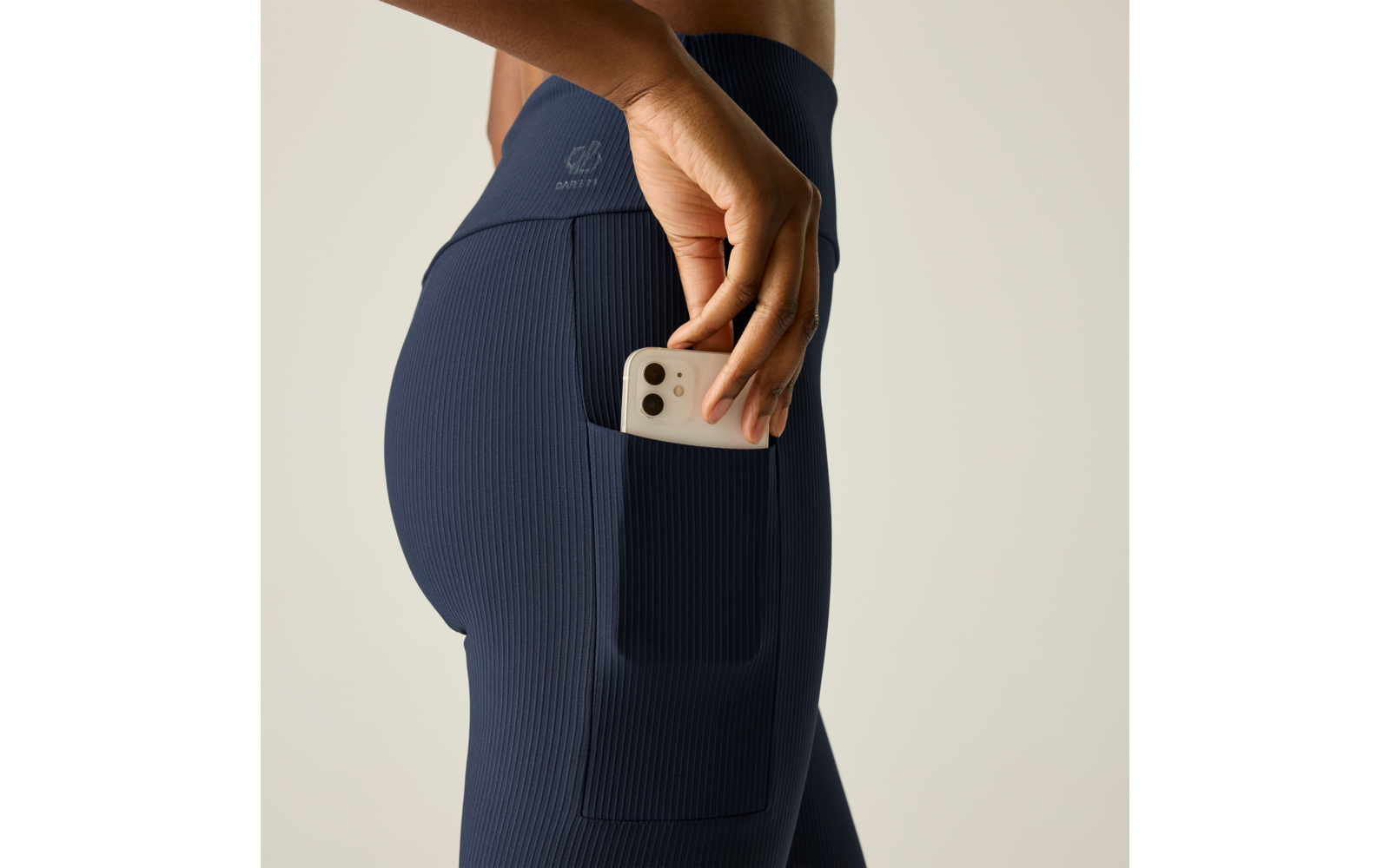 Primer plano de una persona que mete un teléfono inteligente blanco en el bolsillo lateral de unos leggings azul marino acanalados