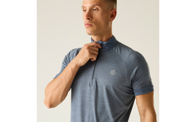 Person von Brust bis Kopf, kurze Haare, blaues kurzärmeliges Funktionsshirt mit kurzem Reißverschluss und kleinem Logo auf der Brust, eine Hand an der Reißverschlussleiste, heller einfarbiger Hintergrund