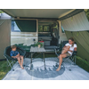 Zwei Männer sitzen vor einem Camper-Van mit geöffnetem Vorzelt, ein Campingtisch steht zwischen ihnen