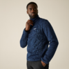 Persoon draagt een blauwe fleece-trui met klein wit logo op de borst, één hand in de zak, de andere raakt de kraag, kijkt opzij tegen een lichte egale achtergrond