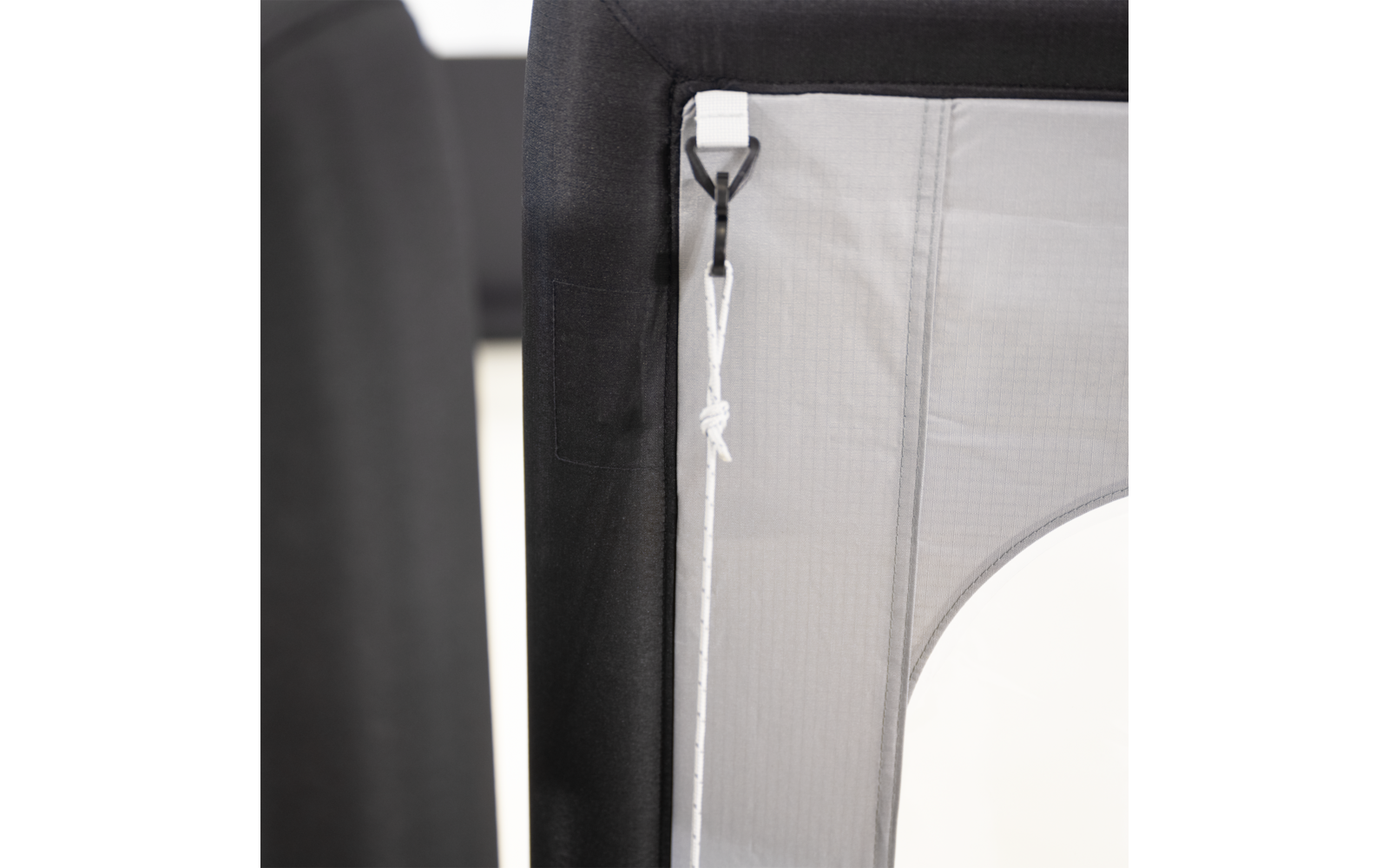 Nahaufnahme eines schwarzen Rahmens mit grauem Stoffeinsatz, an dem eine weiße Schnur mit Knoten an einem weißen Kunststoffhaken befestigt ist