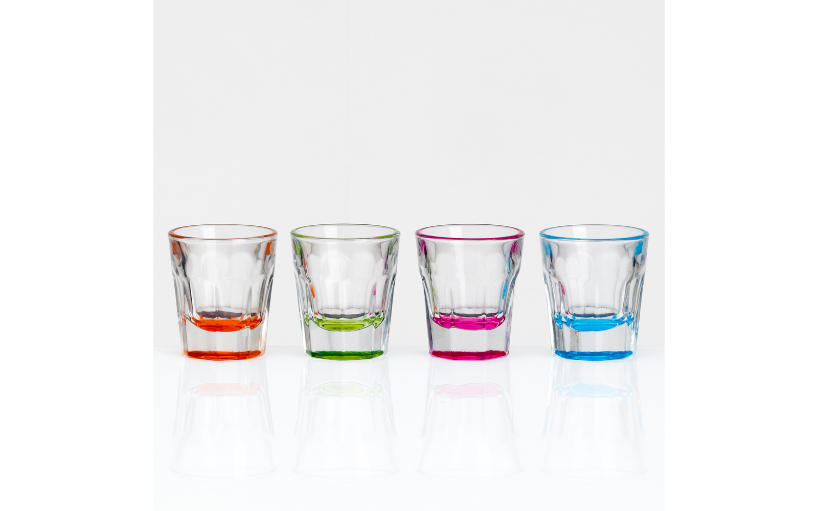 Four clear shot glasses with colored bases (orange, green, pink, blue) lined up on a white background with reflections