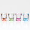 Four clear shot glasses with colored bases (orange, green, pink, blue) lined up on a white background with reflections