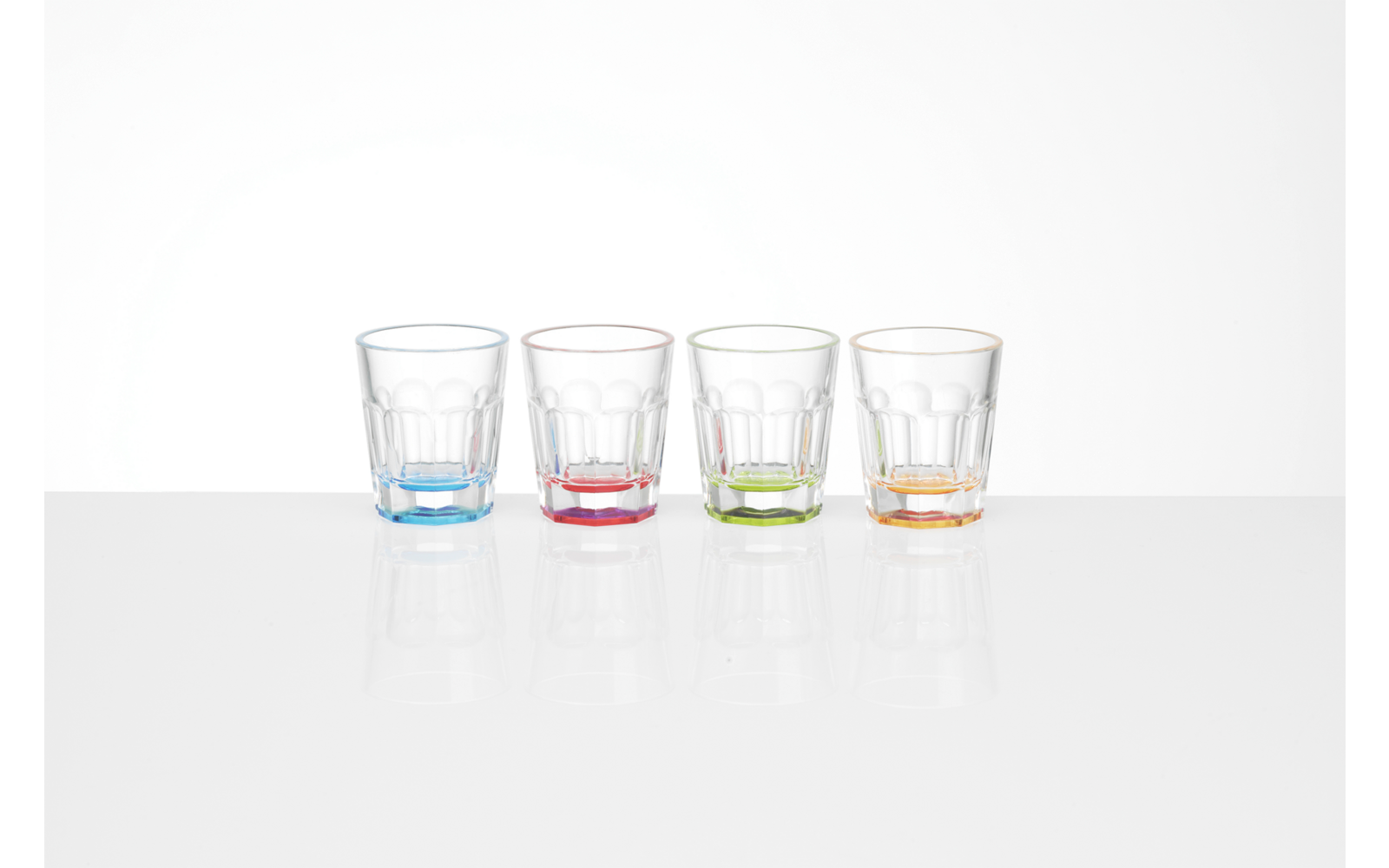 Four transparent empty glasses with colored bases (blue, red, green, orange) side by side on a white surface with reflections