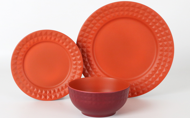 Dos platos naranja con un borde con patrón triangular (uno grande, uno pequeño) colocados verticalmente detrás de un cuenco rojo sobre fondo blanco