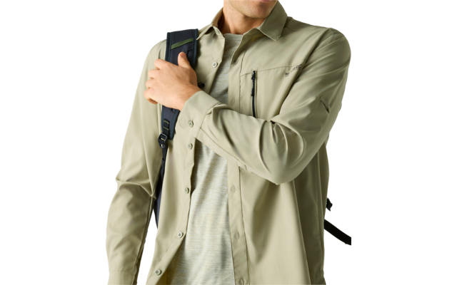 Oberkörper einer Person in hellem khakigrünen Hemd über einem T‑Shirt, die einen Rucksackriemen an der Schulter hält