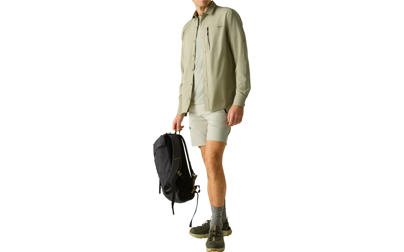 Stehender Mann in hellgrünem Hemd, hellen Shorts und Wanderschuhen, trägt schwarzen Rucksack in der rechten Hand, heller Hintergrund