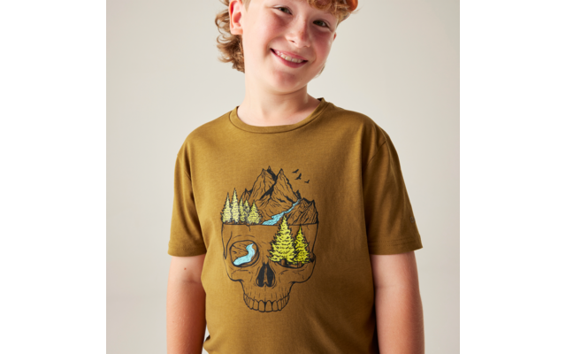 Oberkörper einer lächelnden Person in olivgrünem T‑Shirt mit Totenkopfmotiv, in dem Berge, Bäume, ein Fluss und Vögel abgebildet sind