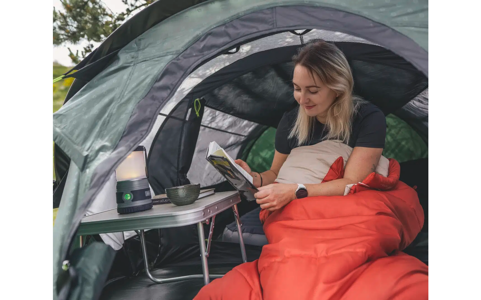 Frau sitzt in einem Campingzelt mit Laptop auf dem Tisch, eingehüllt in eine rote Decke
