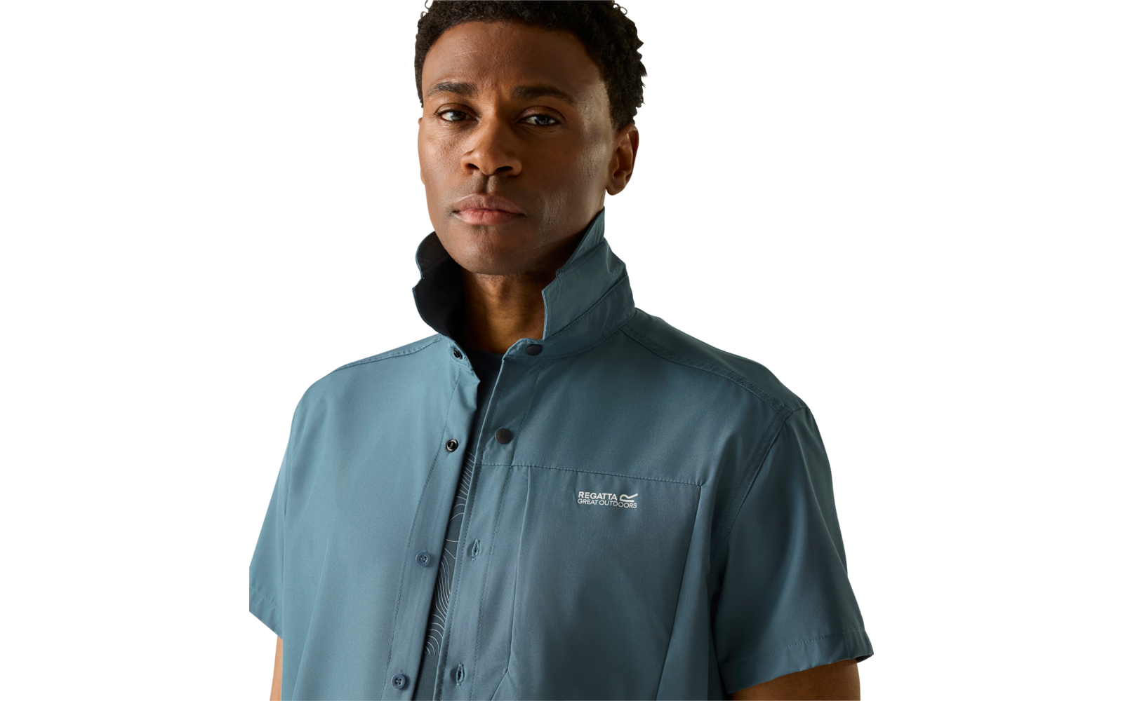 Person mit kurzen lockigen Haaren trägt blaugrünes, kurzärmeliges Hemd mit hochgestelltem Kragen vor hellem Hintergrund