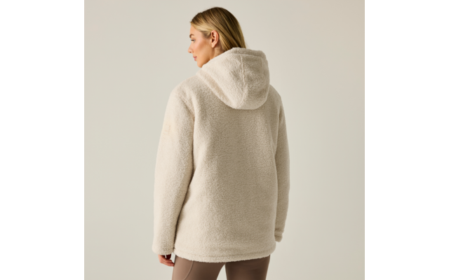 Vista posteriore di una persona con capelli biondi che indossa una giacca teddy in pile beige chiaro con cappuccio e leggings marroni su uno sfondo chiaro e neutro