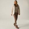 Persona con capelli biondi lunghi in piedi, indossa una giacca in pile beige chiaro con fodera rosa, una maglia beige, leggings marroni e stivaletti marroni su sfondo chiaro uniforme