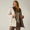 Donna con giacca sherpa crema con cappuccio, giacca aperta che mostra fodera trapuntata marrone, indossa maglia beige e leggings marroni, in piedi davanti a sfondo neutro e tiene i bordi della giacca