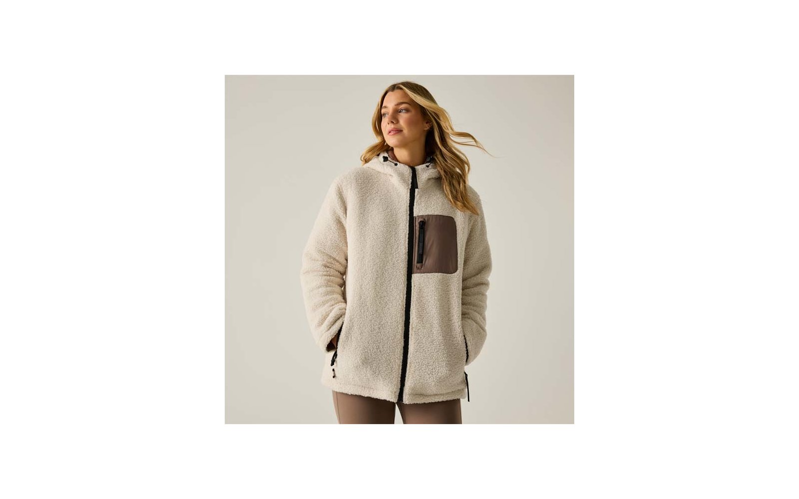 Donna con giacca sherpa color crema con cappuccio, cerniera frontale, tasca sul petto marrone e tasche laterali