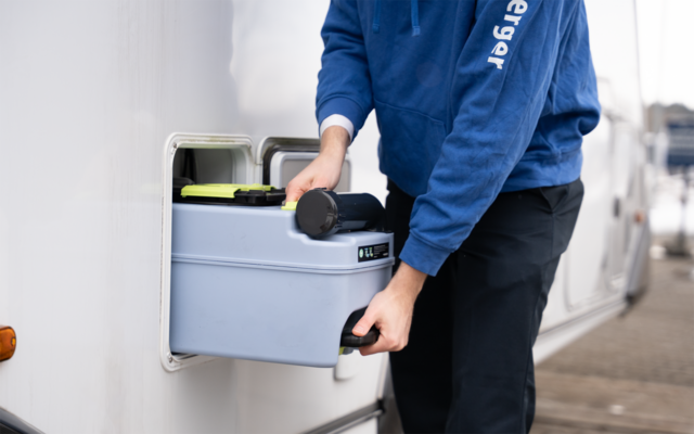 Person in blauem Kapuzenpullover zieht eine tragbare Campingtoilette aus dem Außenfach eines Wohnmobils