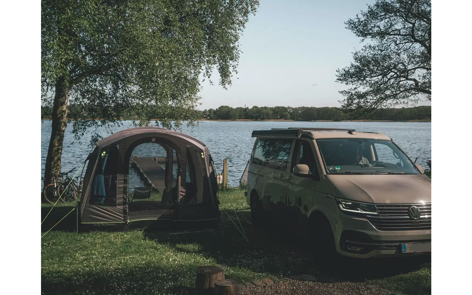Auto mit angebautem großen Zelt an einem Gewässer mit Bäumen im Hintergrund